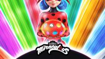 A girl dressed in a ladybug suit is holding a glowing red ball in her hands and standing in front of a rainbow background.